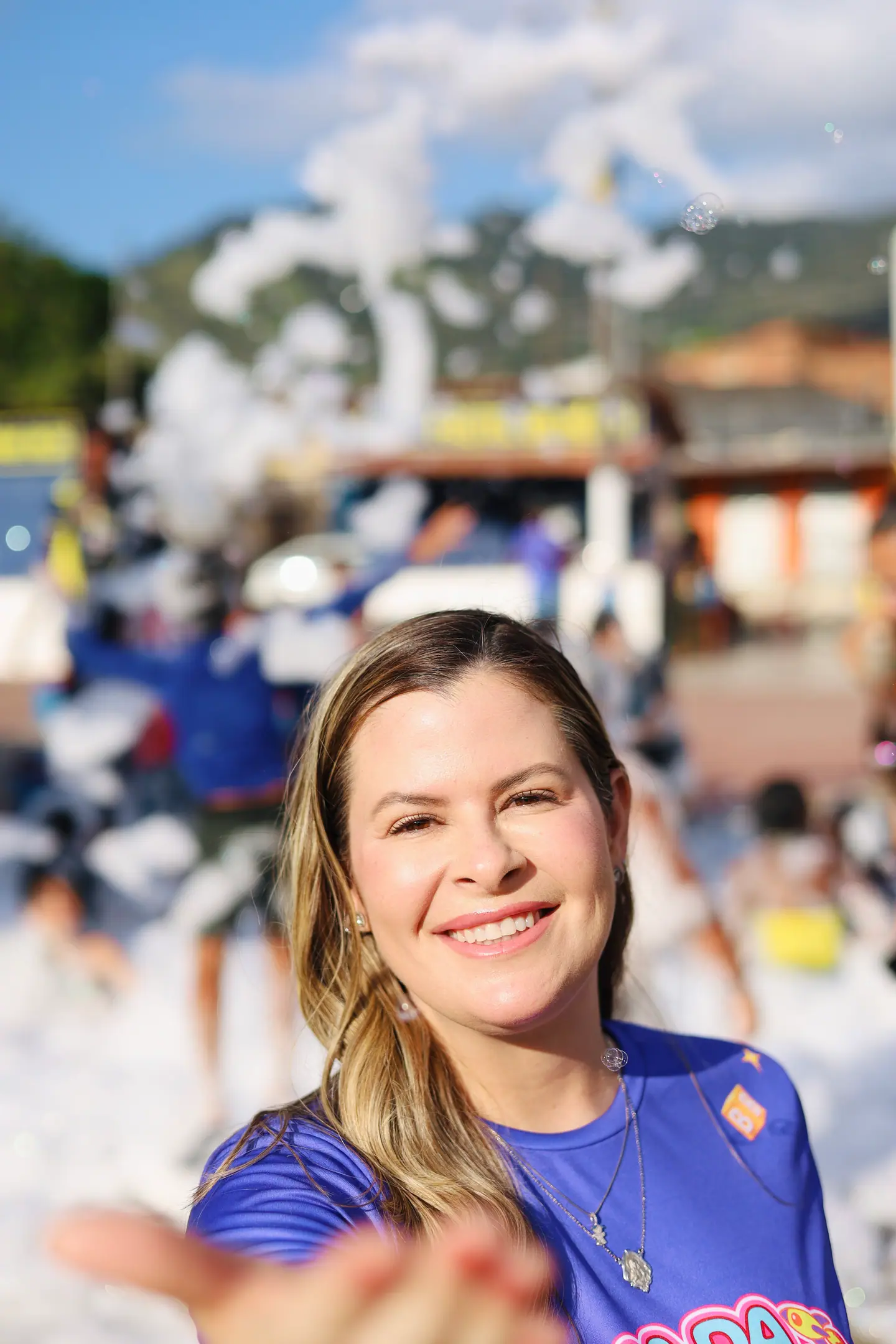 Mulher sorri em primeiro plano com a festa da espuma ao fundo