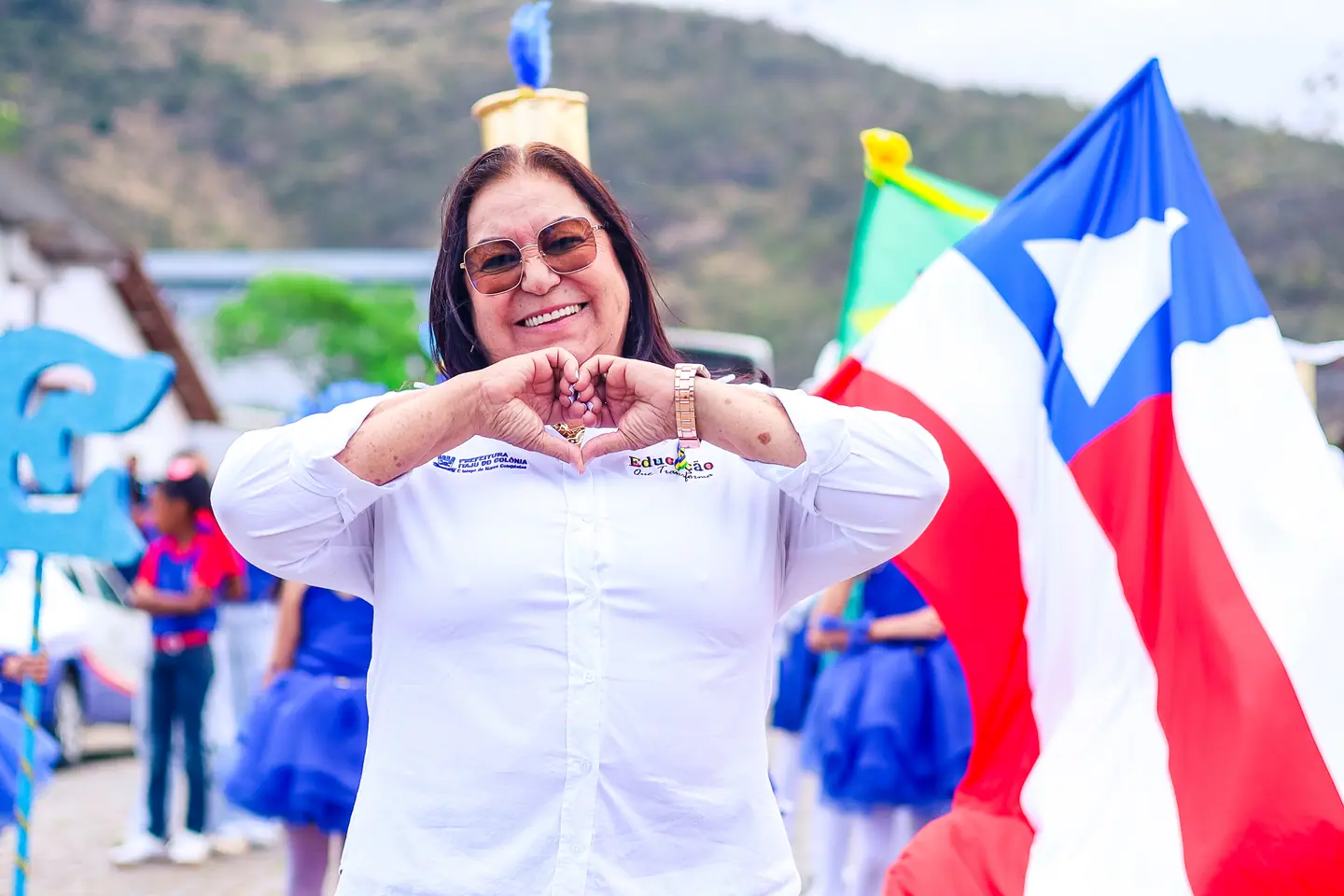 Mulher faz coração com as mãos ao lado da bandeira da Bahia em desfile