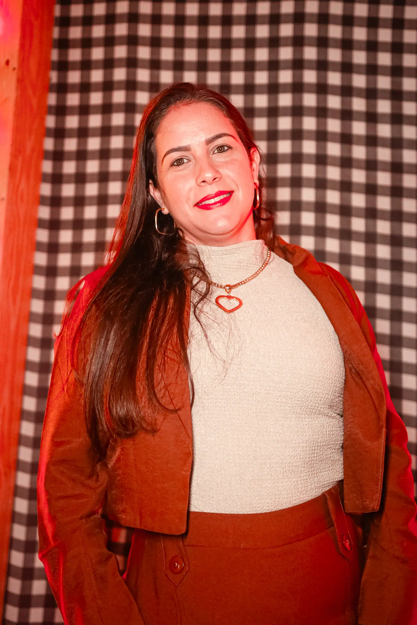 Retrato de mulher sorridente de blazer terracota diante de fundo xadrez