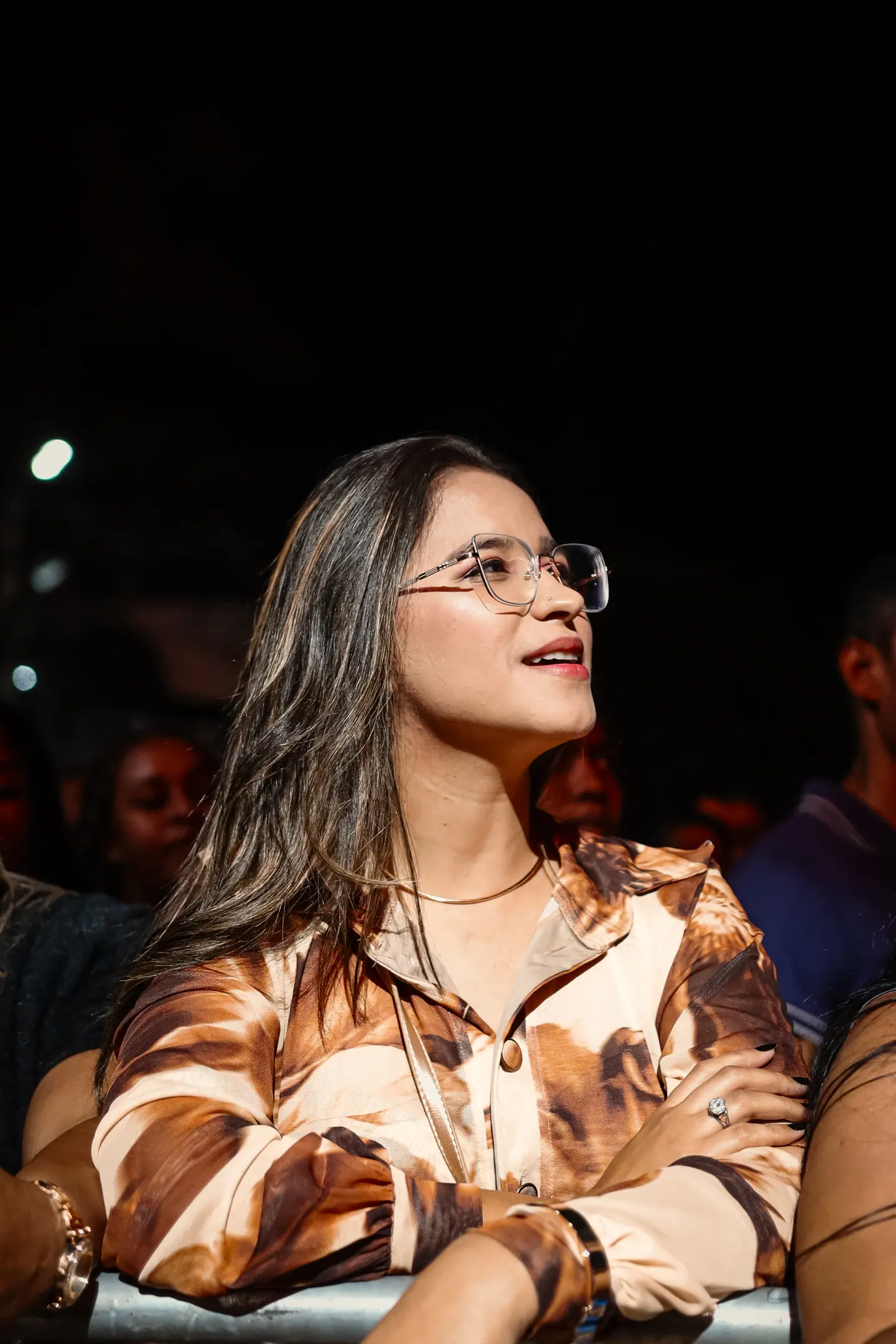 Jovem de óculos assiste ao show na grade, iluminada pelo palco